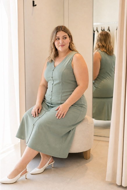 Plus-size женщина садится в зелёном платье А-силуэта и проверяет свободу по животу